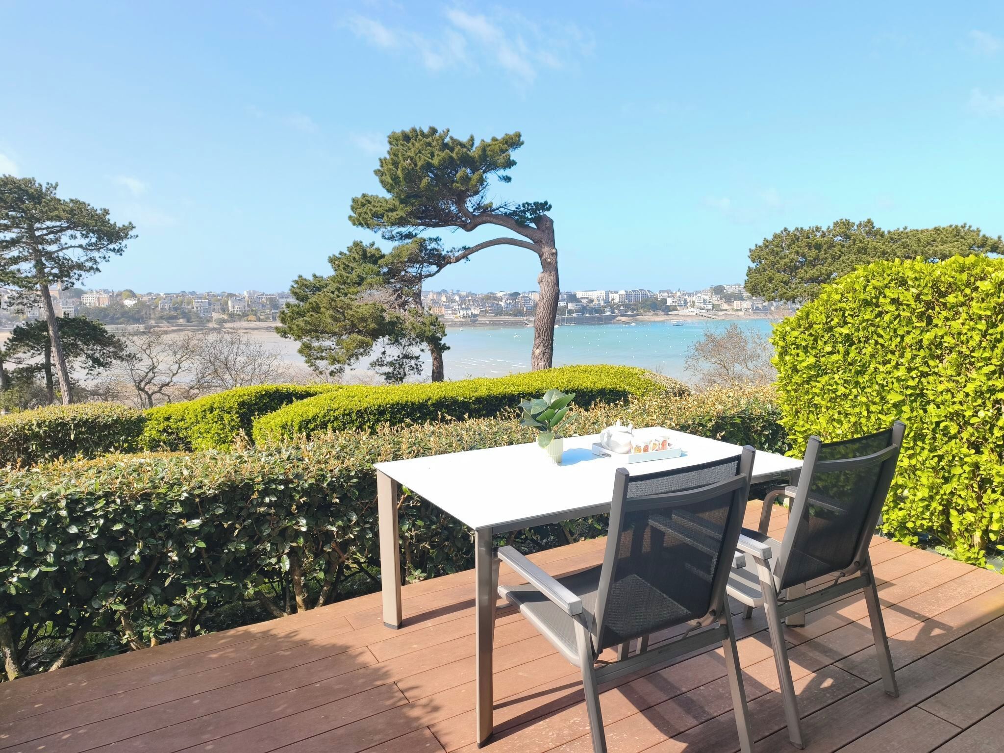 A table with chairs on a wooden deck overlooking a coastal cityscape.