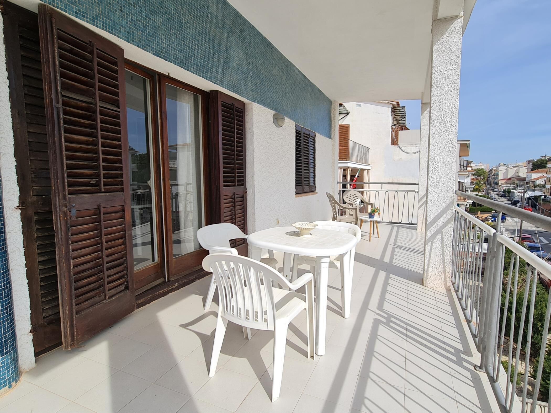 Een balkon met een tafel en stoelen, een uitzicht op de straat, en een gebouw met blauw betegelde muren.