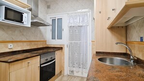 Une cuisine compacte équipée d’un four à micro-ondes, d’un four, d’un évier et de meubles de rangement en bois.