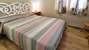 Une chambre à coucher comprenant un lit, une table de chevet, une lampe, une fenêtre avec des rideaux et une œuvre d’art murale.