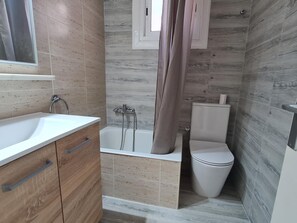 A bathroom with a bathtub, toilet, and sink, featuring wooden and tiled walls.