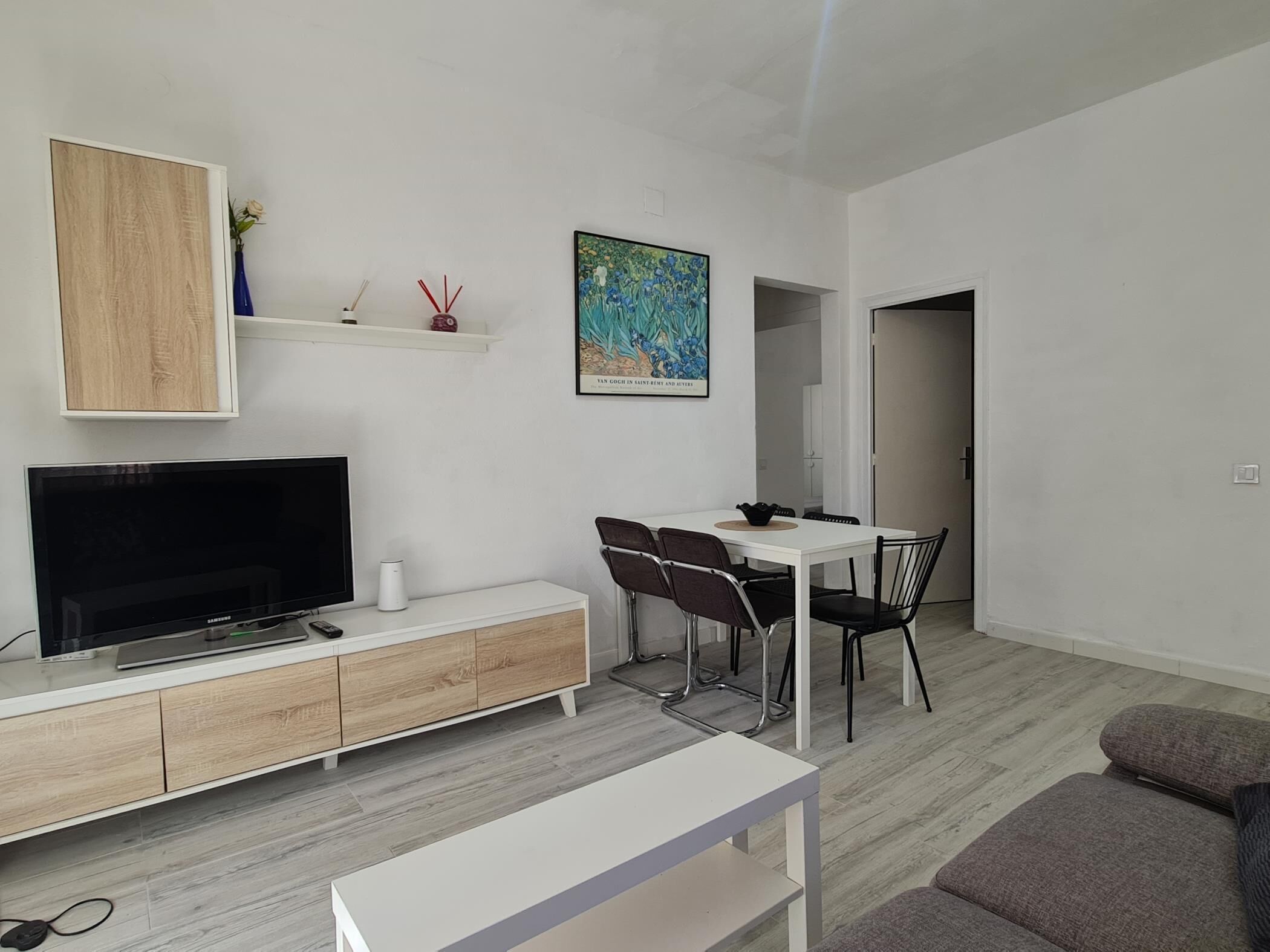 Ein modernes Wohnzimmer mit Fernseher, weißen Möbeln, einem Essbereich und einem Gemälde an der Wand.