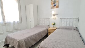 Habitación con dos camas, un armario, una mesita de noche con lámpara y una obra de arte colgada en la pared.