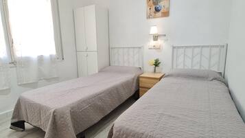 A room with two beds, a wardrobe, a nightstand with a lamp, and a wall-mounted artwork.