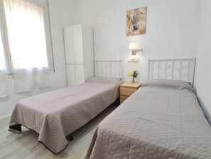 A room with two beds, a wardrobe, a nightstand with a lamp, and a wall-mounted artwork.