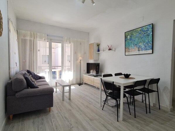 A modern living room with a sofa, dining table, chairs, and a TV.