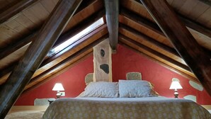 A bedroom with a sloped ceiling, wooden beams, a bed with a patterned bedspread, two bedside lamps, and a stone wall. - Vivelorural El Caminante- Valleseco, private pool (Valleseco)