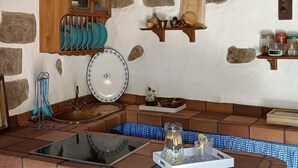 A rustic kitchen with stone walls, wooden shelves, and a tiled floor. - Vivelorural El Caminante- Valleseco, private pool (Valleseco)