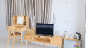A room with a wooden desk, a television, a chair, a small refrigerator, and a curtain. - Baan O Resort (Rayong)
