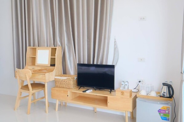A room with a wooden desk, a television, a chair, a small refrigerator, and a curtain. - Baan O Resort (Rayong)