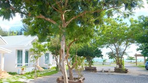 A white building with a covered outdoor area, surrounded by trees and gravel paths. - Baan O Resort (Rayong)