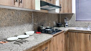 Una cocina con encimeras de granito, armarios de madera, estufa a gas, licuadora y una ventana con persianas.