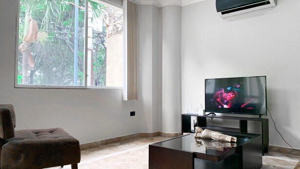Una sala de estar con televisor, sofá y ventana con vistas a zonas verdes.