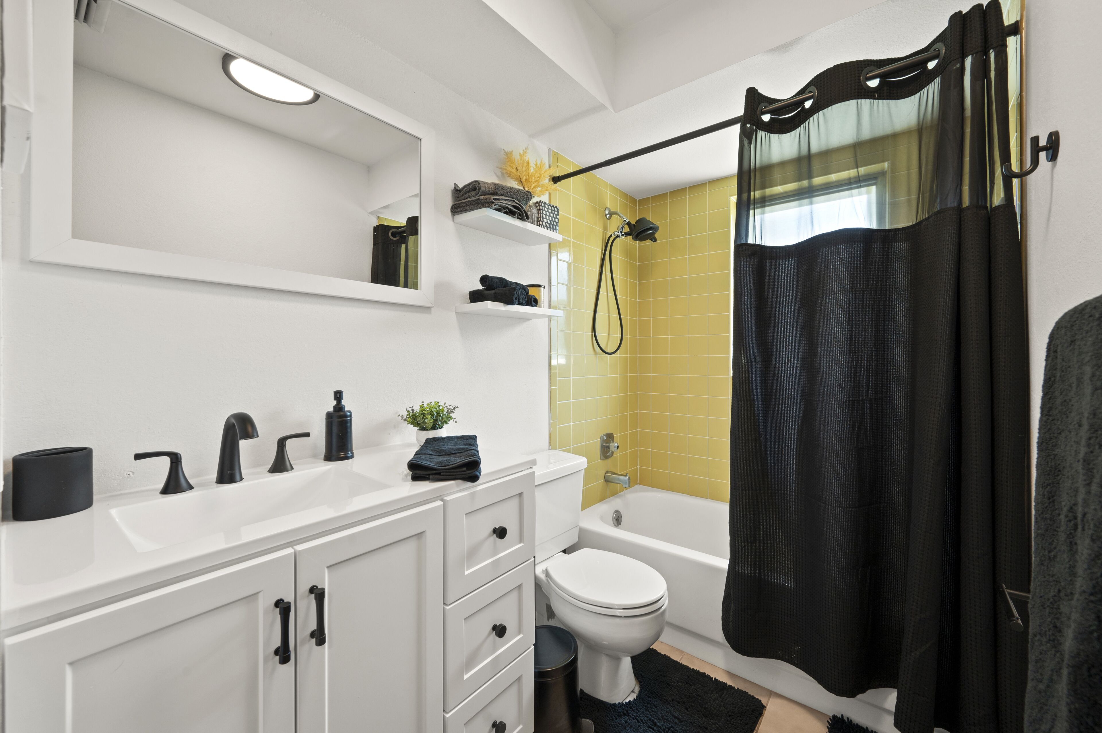 Une salle de bain moderne avec un meuble-lavabo blanc, un rideau de douche noir et une zone de douche carrelée de carreaux jaunes.
