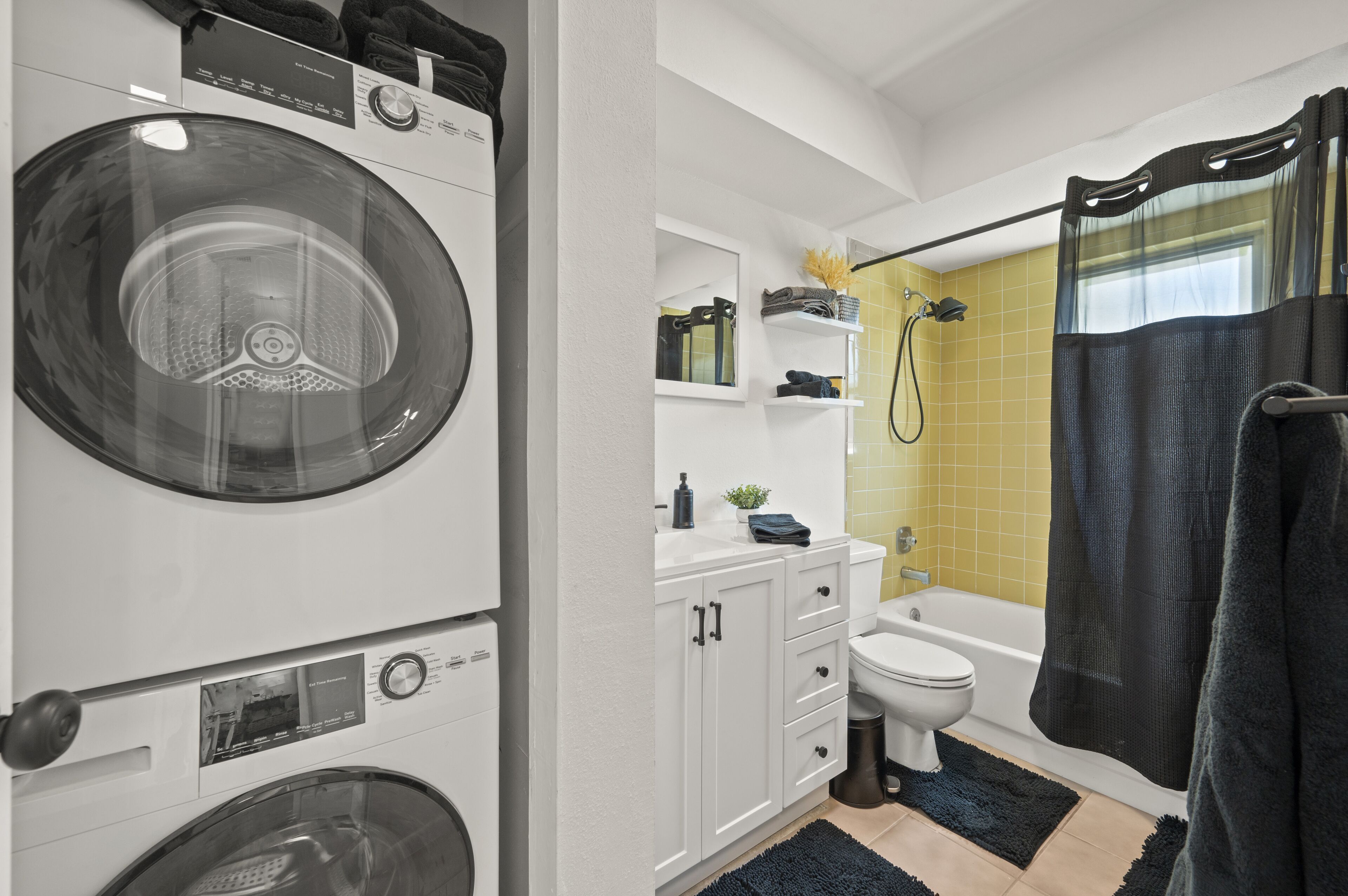 A compact laundry area with a front-loading washer and dryer, a small bathroom with a toilet and sink, and a shower with a curtain.