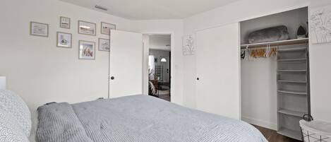 A bedroom with a large bed, a walk-in closet, and a hallway leading to another room.