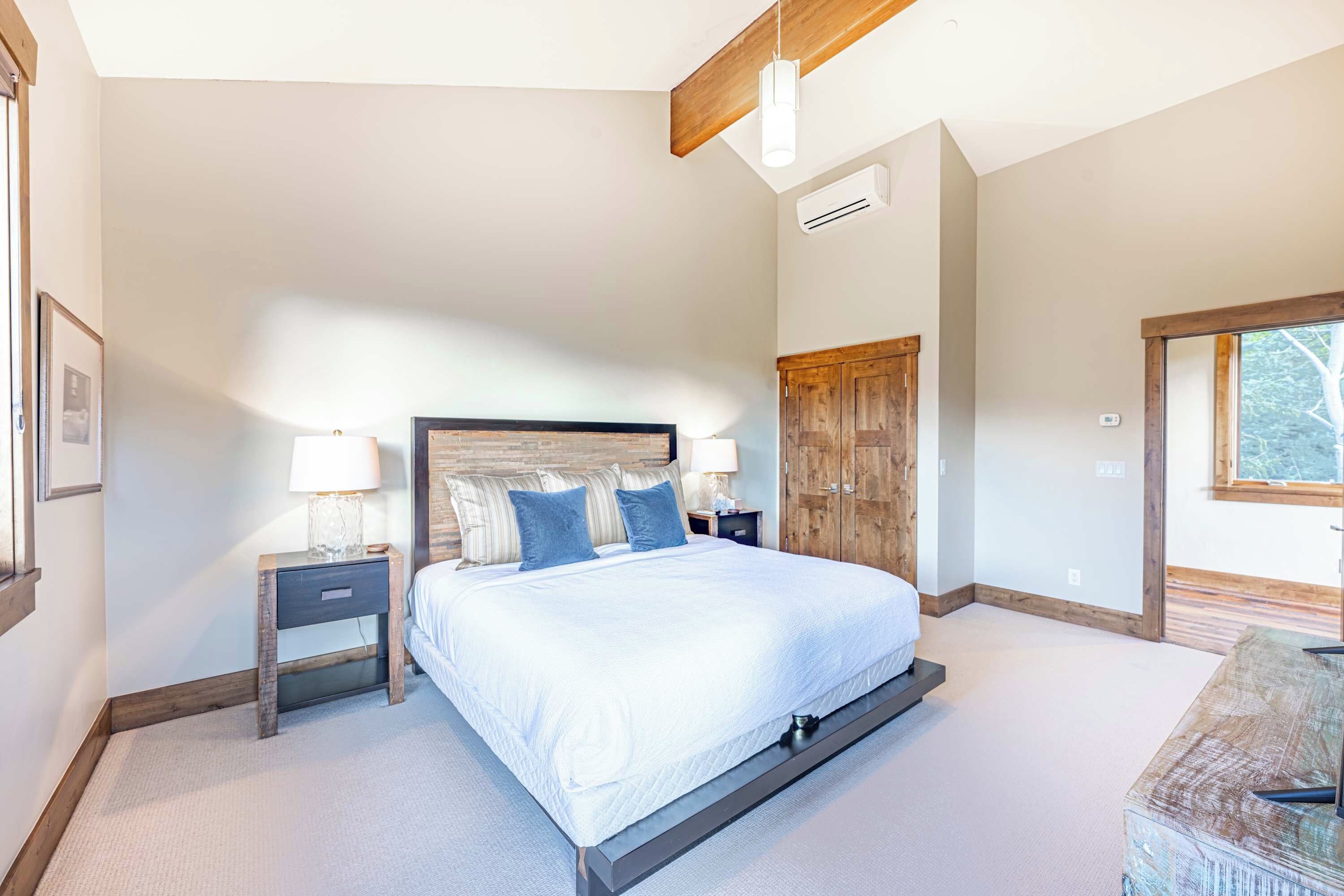 A bedroom with a large bed, wooden headboard, bedside tables with lamps, a wardrobe, and a window.