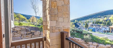 A stone pillar and wooden railing of a balcony with a view of a residential area and hills.