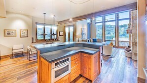 Een moderne keuken met een centraal eiland, houten kastjes en een groot raam met uitzicht op de omgeving.