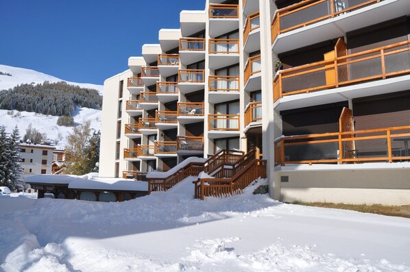 A multi-story hotel with balconies, a snow-covered ground, and a mountainous backdrop. - Cosy apt 4/6 ppl with balcony, near the ski runs (Les Deux Alpes)