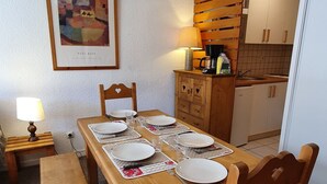 A dining area with a wooden table set for four, a bench, and a chair with a cushion. A framed artwork is on the wall, and a lamp is on a side table. - Cosy apt 4/6 ppl with balcony, near the ski runs (Les Deux Alpes)
