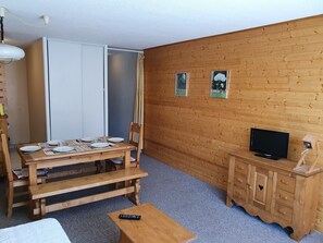 Quarto com uma mesa de madeira posta para dois, uma televisão sobre um armário de madeira e uma porta deslizante.