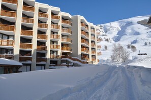 Ett hotell med flera våningar, balkonger, ett snötäckt landskap och en skidbacke i bakgrunden.