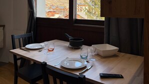 A dining area with a table set for two, a window with a view of a snowy landscape, and a wooden cabinet. - Les 2 Alpes studio 2 ppl with ski station view (Les Deux Alpes)