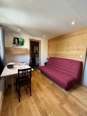 Un ambiente compatto con pavimento in legno, un divano rosso, un tavolo da pranzo con sedie, una TV a parete e pannelli di legno.