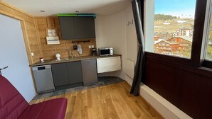 A compact kitchen with a built-in microwave, a sink, and a window with a view of buildings. - Les 2 Alpes studio 2 ppl with ski station view (Les Deux Alpes)