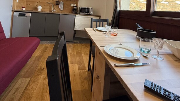 A compact kitchen with wooden cabinets, a dining table set for two, and a view of a snowy landscape through a window. - Les 2 Alpes studio 2 ppl with ski station view (Les Deux Alpes)