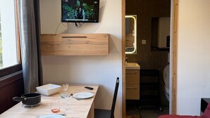 A hotel room with a dining table, chairs, a TV on the wall, a bed, and a kitchen area visible through an open door. - Les 2 Alpes studio 2 ppl with ski station view (Les Deux Alpes)