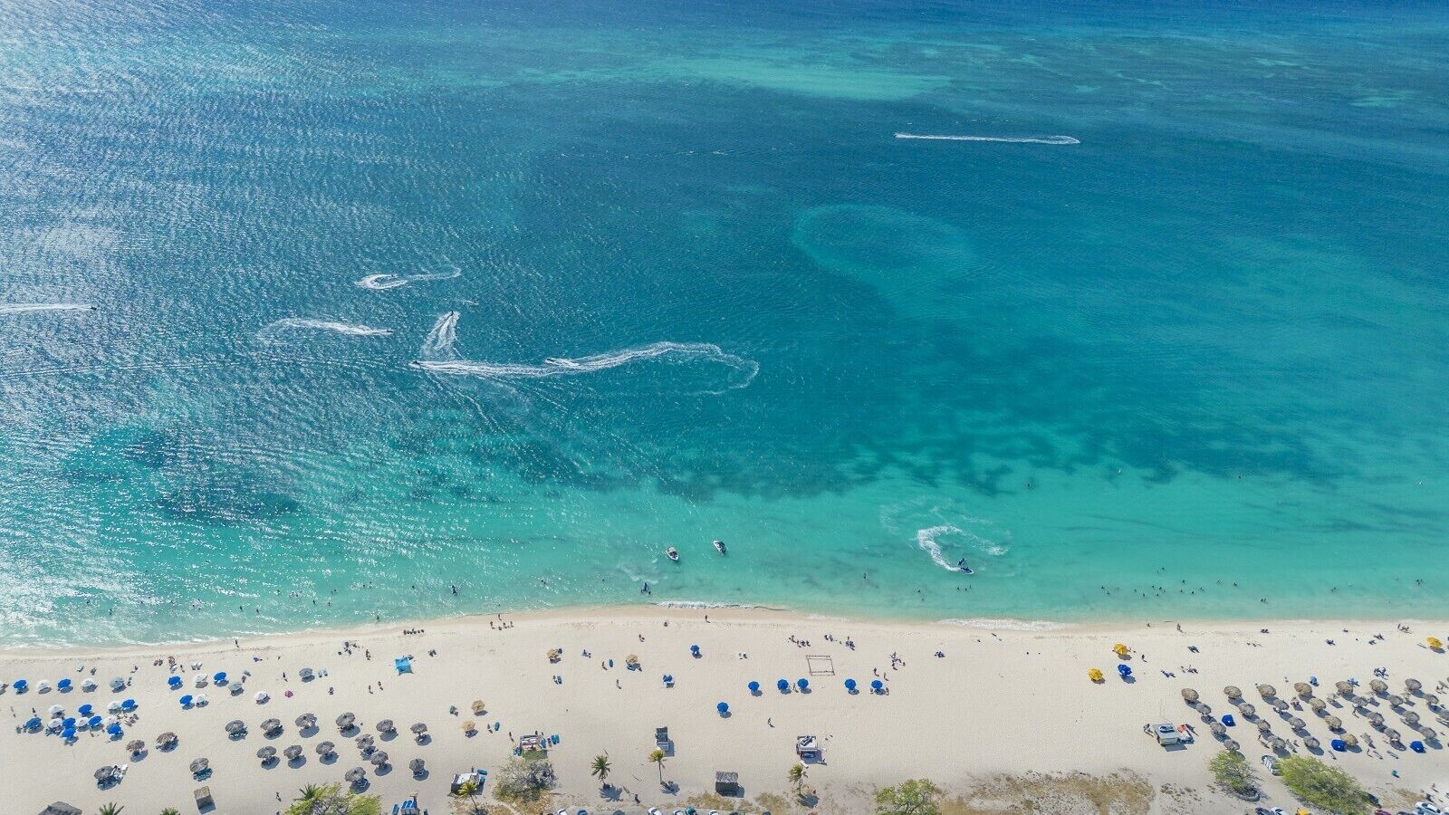 Ein Strand mit klarem türkisblauem Wasser, einem Sandstrand und zahlreichen Sonnenschirmen.