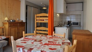 Una habitación acogedora con una litera de madera, una mesa de comedor con mantel estampado, una zona de cocina con microondas y un armario.