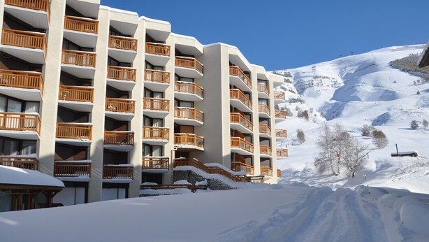 Un hotel de varios pisos con balcones, un paisaje nevado y una pista de esquí al fondo.