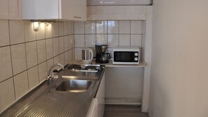 Una cocina compacta con un lavamanos de acero inoxidable, una cafetera y un microondas.