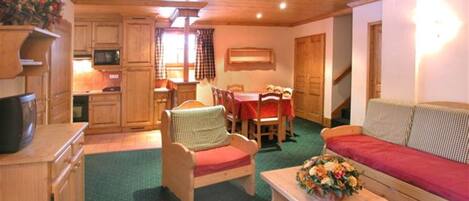 A cozy room with a wooden ceiling, a dining area with a table and chairs, a sofa, and a kitchen area with cabinets and a microwave.