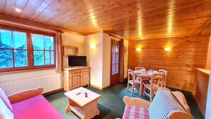Un interior de cabaña acogedor, con techo de madera, televisor, mesa de comedor con sillas y un sofá.