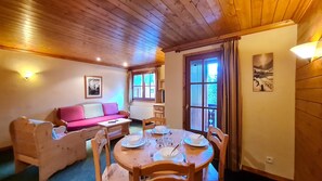 A cozy room with a wooden ceiling, a pink sofa, a dining table set for four, and a window with curtains. - Alpina Lodge - 21 - Appart proche pistes - 4 pers (Les Deux Alpes)