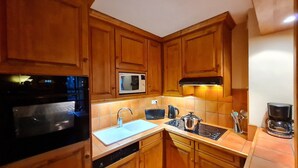 Una cocina compacta con armarios de madera, microondas, estufa, fregadero y cafetera.