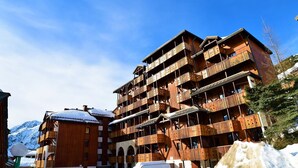 A multi-story wooden building with balconies, likely a hotel, with snow on the ground. - Andromede - 35 - Studio coeur station - 4 pers (Les Deux Alpes)