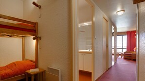 A room with a bunk bed, a small table, a radiator, and a view of a bathroom with a sink and cabinets.