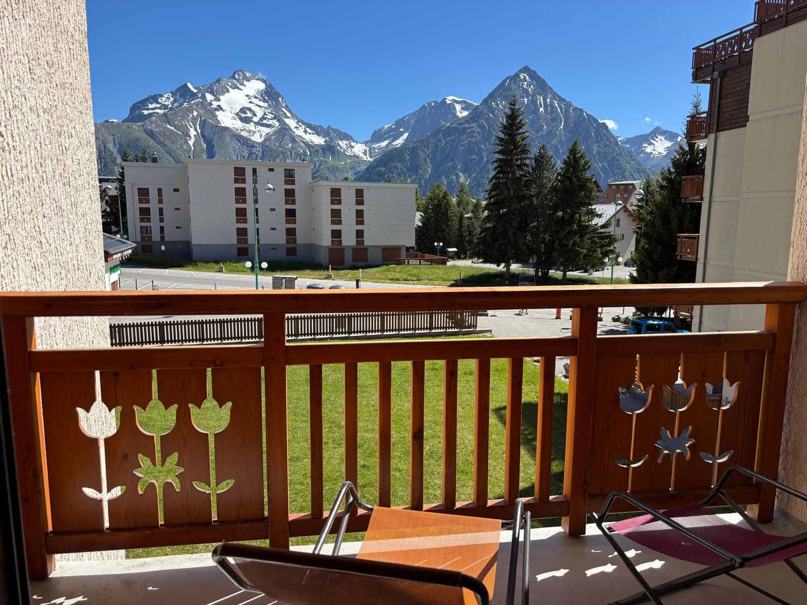 A balcony with a view of snow-capped mountains, a wooden fence with floral cutouts, and a table with chairs.