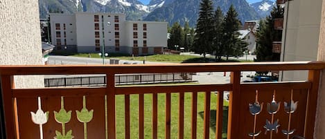 Un balcón con vistas a montañas nevadas, una valla de madera con adornos florales y una mesa con sillas.