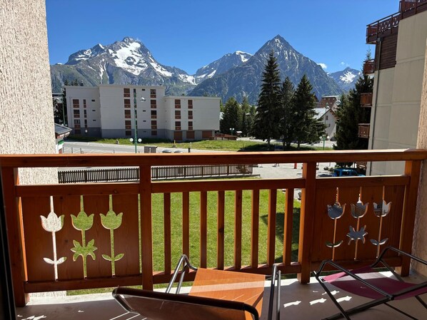 Ein Balkon mit Blick auf schneebedeckte Berge, ein Holzzaun mit floralen Ausschnitten und ein Tisch mit Stühlen.