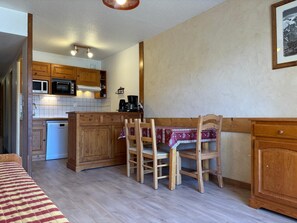 Une cuisine compacte dotée de meubles en bois, d’un four à micro-ondes, d’une machine à café et d’une table à manger avec des chaises.