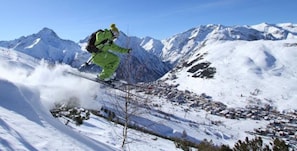 Un skieur en mouvement sur une pente enneigée, avec une chaîne de montagnes en arrière-plan.