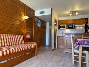 Une pièce chaleureuse avec un canapé en bois, une table à manger recouverte d’une nappe à motifs, des meubles en bois et un four à micro-ondes.
