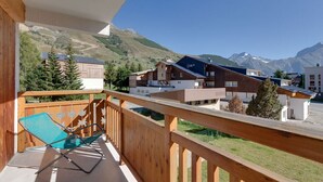 A balcony with a wooden railing, a blue chair, and a view of buildings and mountains.