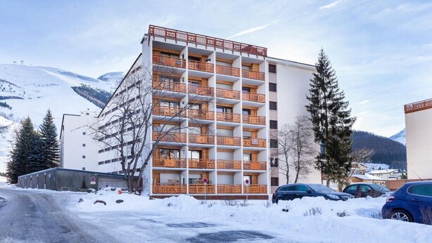 A multi-story hotel with balconies, a parking area, and snow-covered surroundings.